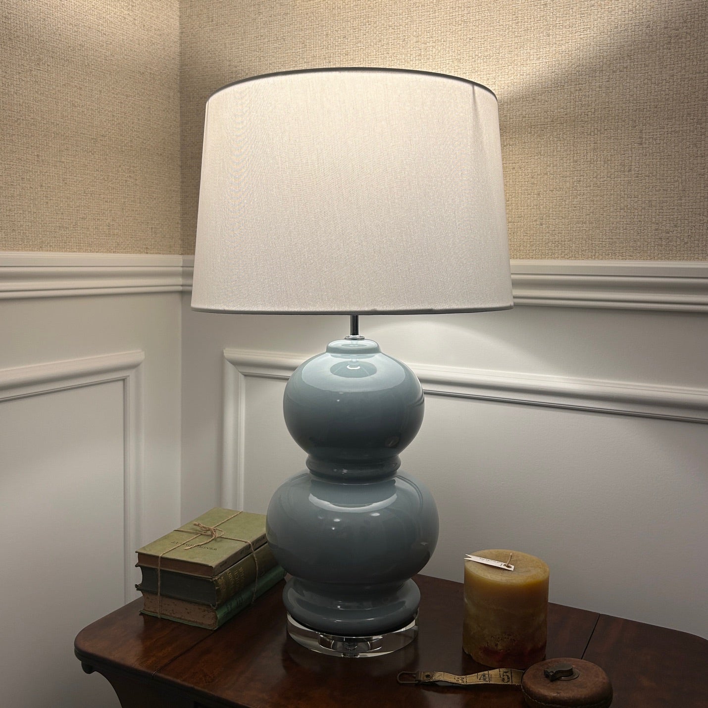 Blue ceramic lamp with a white shade on a wooden table against a neutral wall