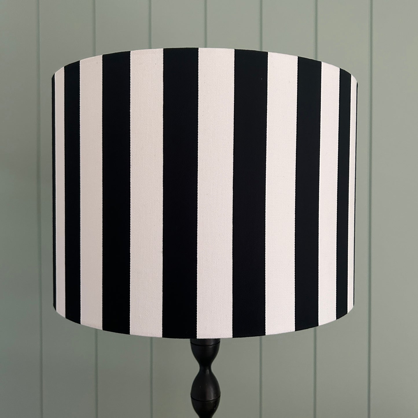 Black and white striped lampshade on a wooden stand against a green wooden panel background