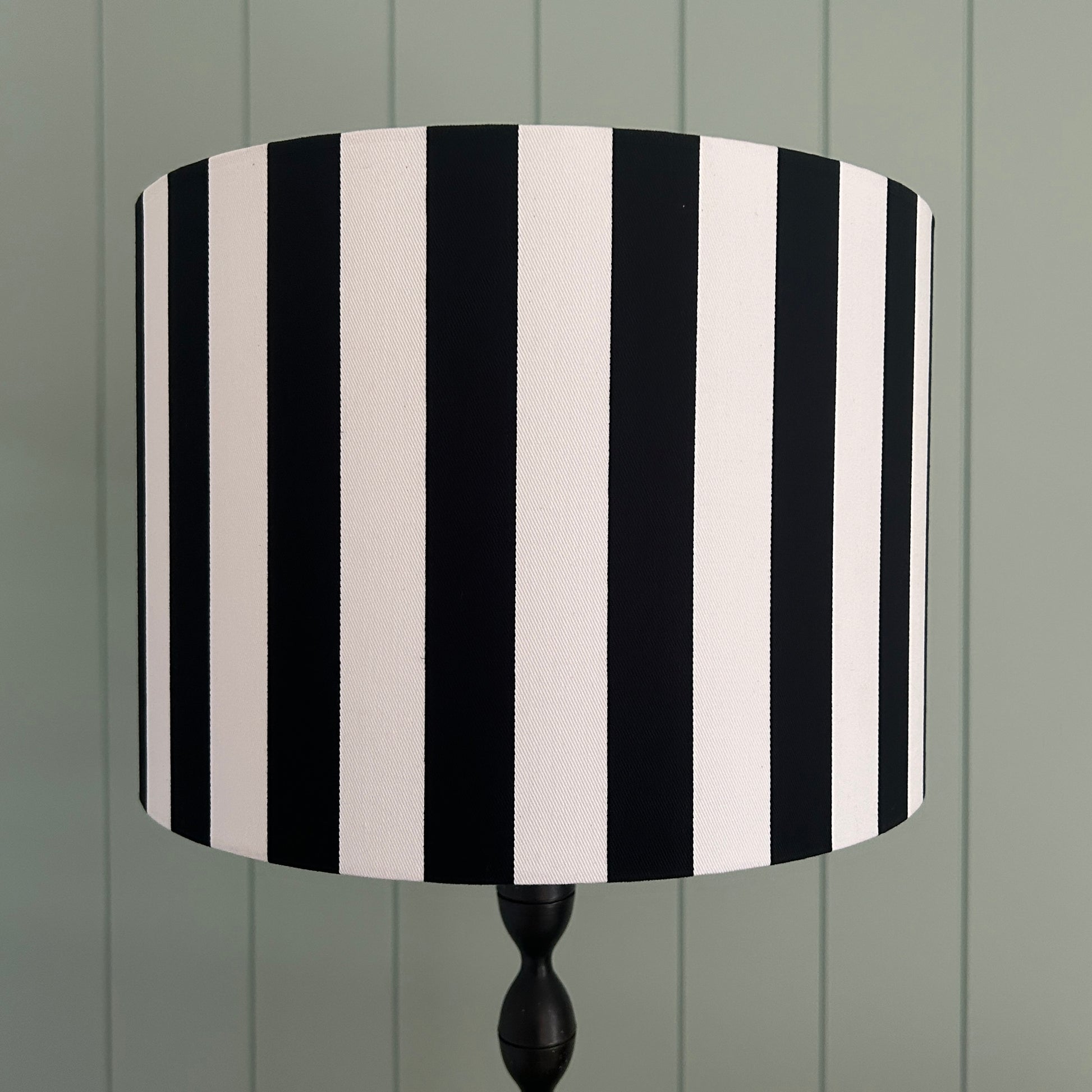 Black and white striped lampshade on a wooden stand against a green wooden panel background