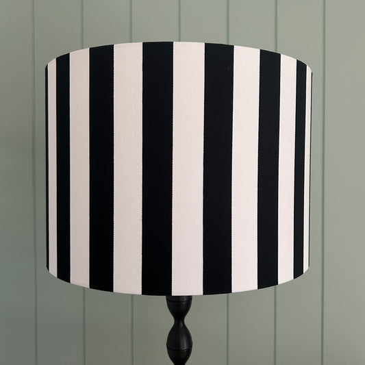 Black and white striped lampshade on a wooden stand against a green wooden panel background
