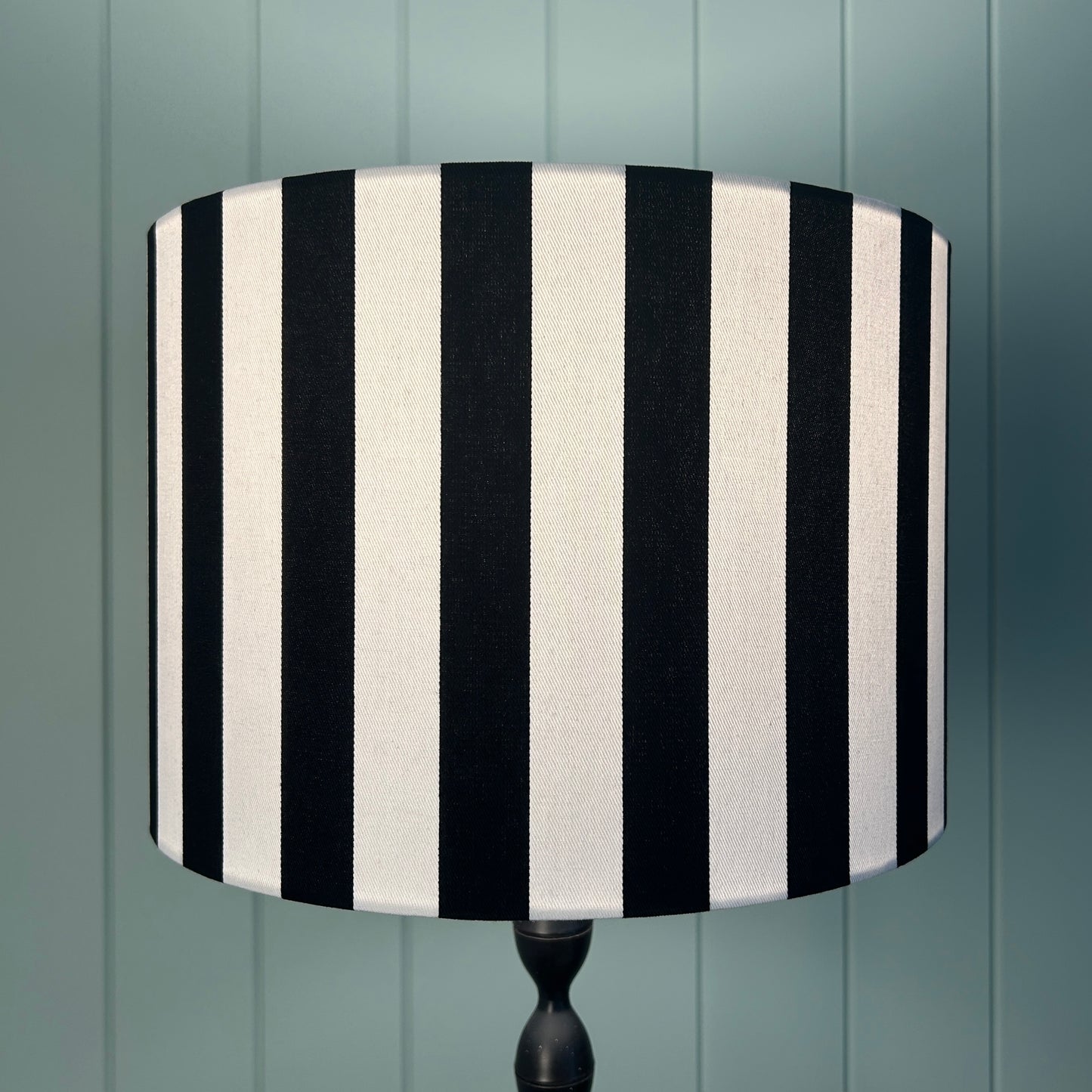 Black and white striped lampshade on a lamp stand against a panelled wall