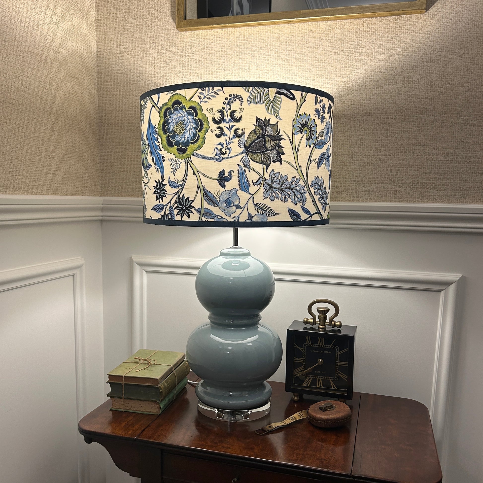 Decorative lamp with floral chintz pattern shade on a wooden table against a neutral wall.