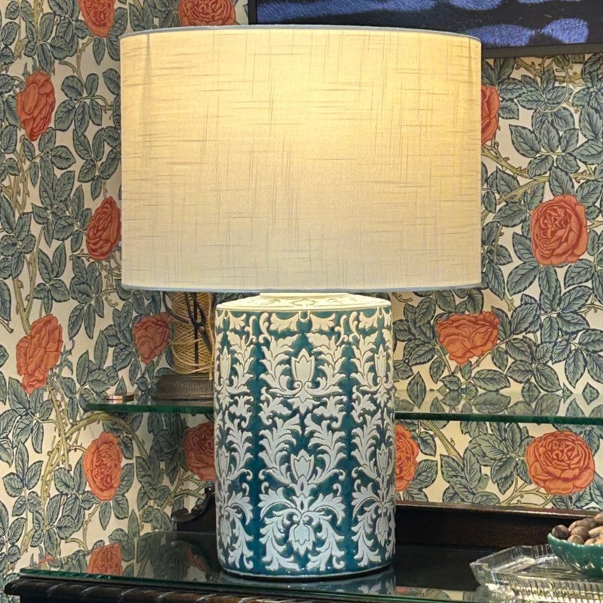 Decorative lamp with a patterned base on a table against floral wallpaper.