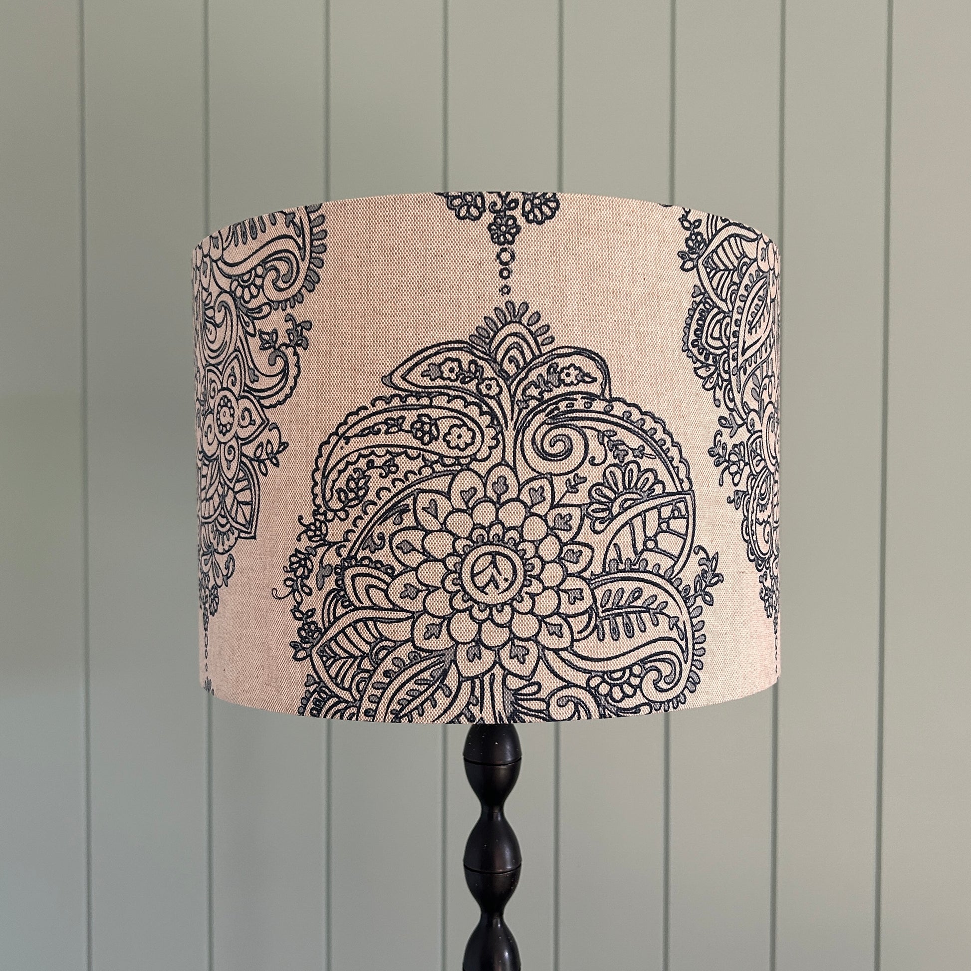 Decorative lampshade with paisley pattern against a wooden panel background