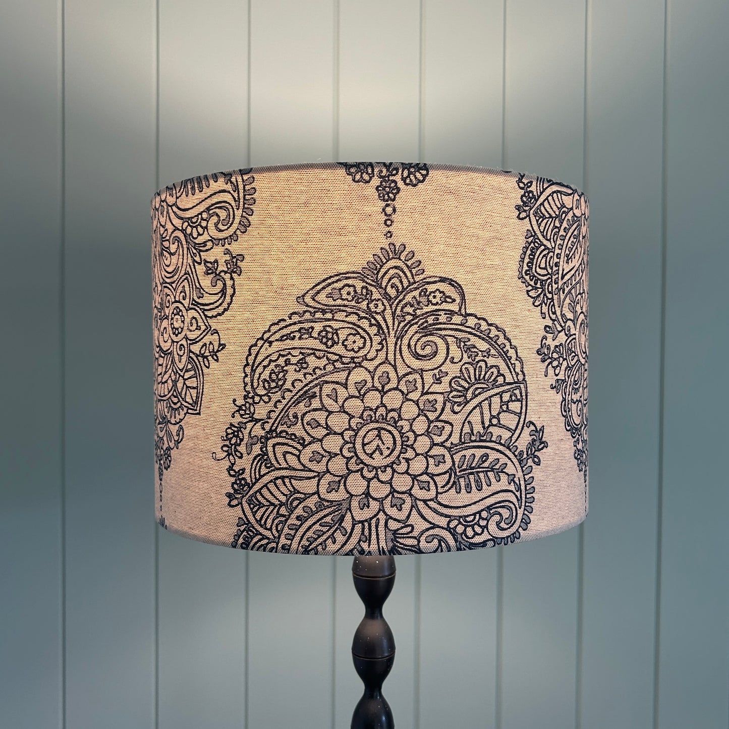 Decorative lampshade with paisley pattern against a wooden panel background