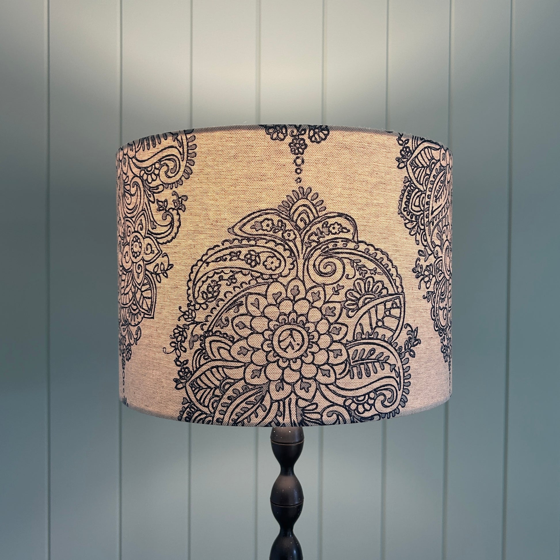 Decorative lampshade with paisley pattern against a wooden panel background