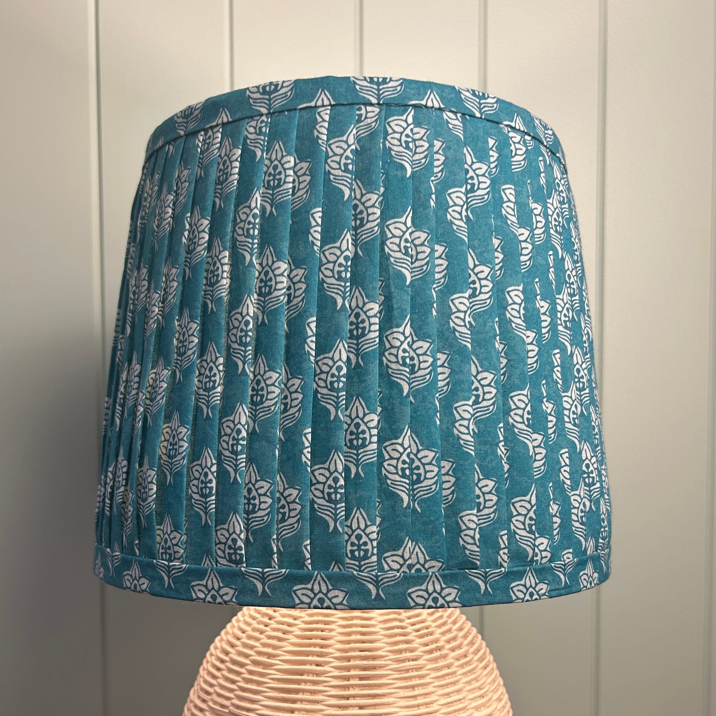 Blue patterned pleated lampshade on a wooden stand against a paneled wall