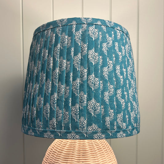 Blue patterned pleated lampshade on a wooden stand against a paneled wall