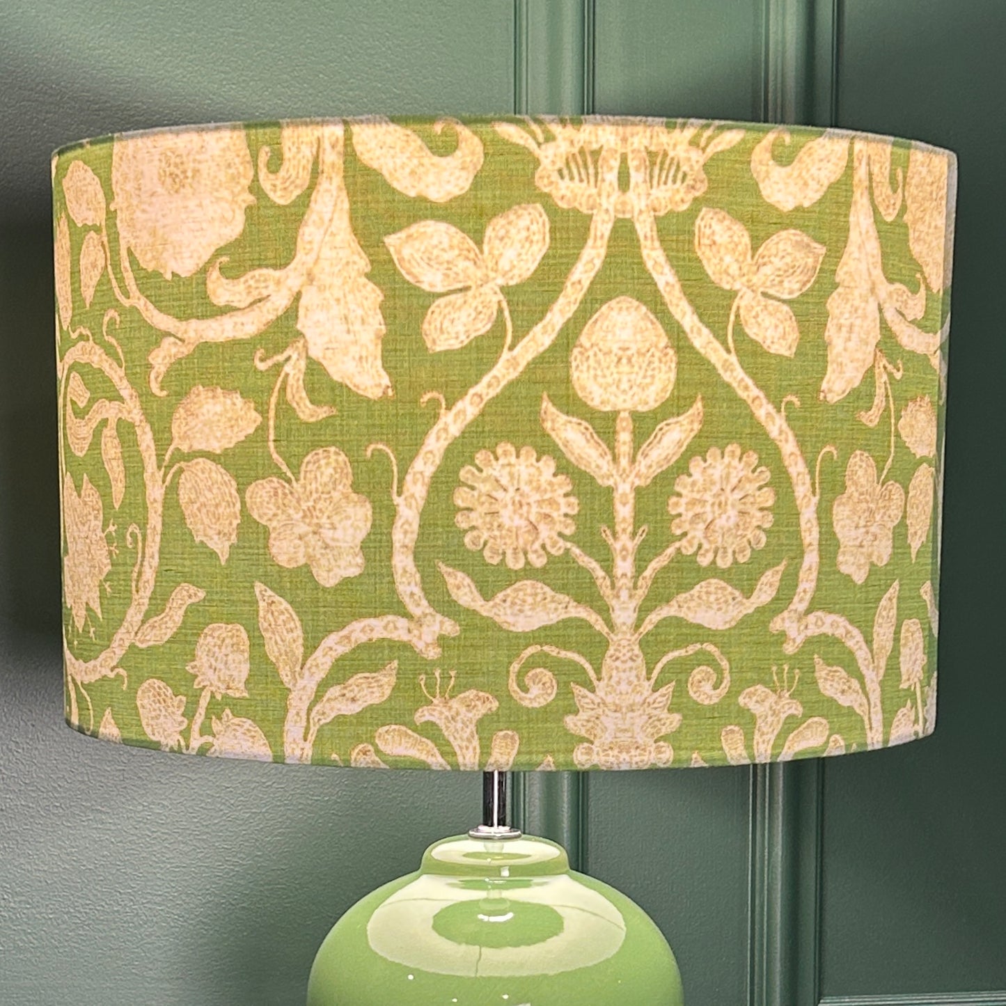 Green lamp with floral patterned shade against a dark green wall.