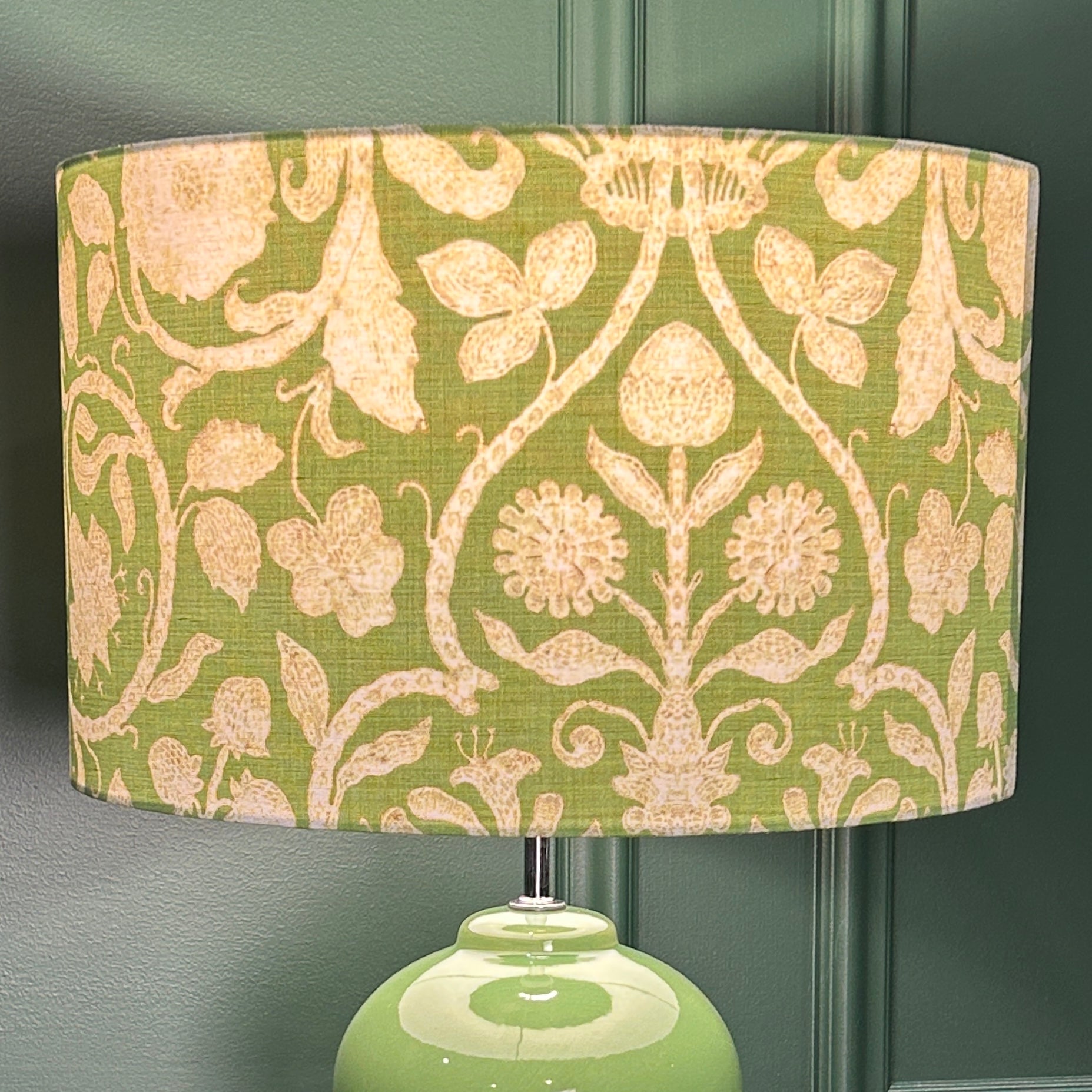 Green lamp with floral patterned shade against a dark green wall.