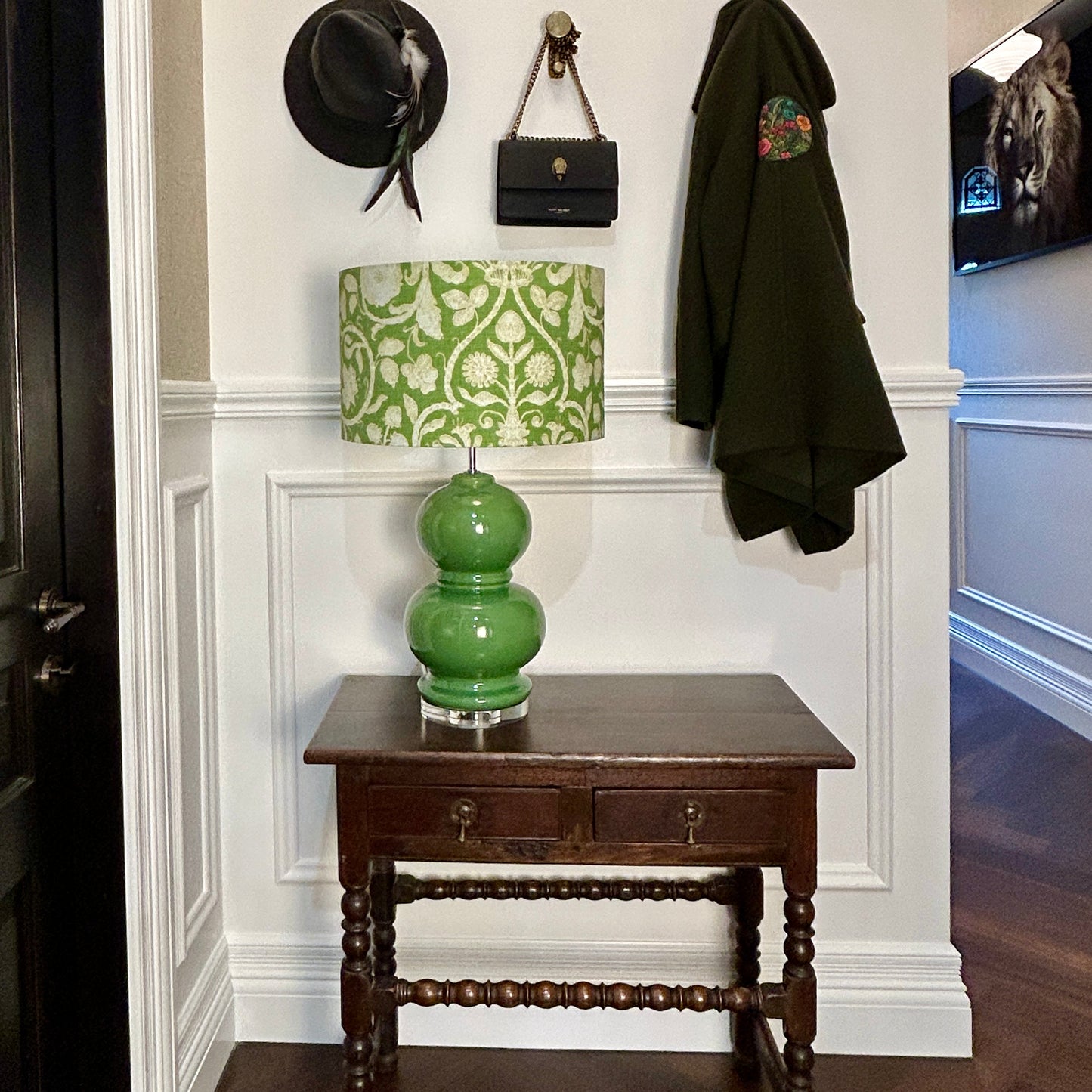 Spring green lamp on a wooden table against a white wall with a coat and hat hanging above