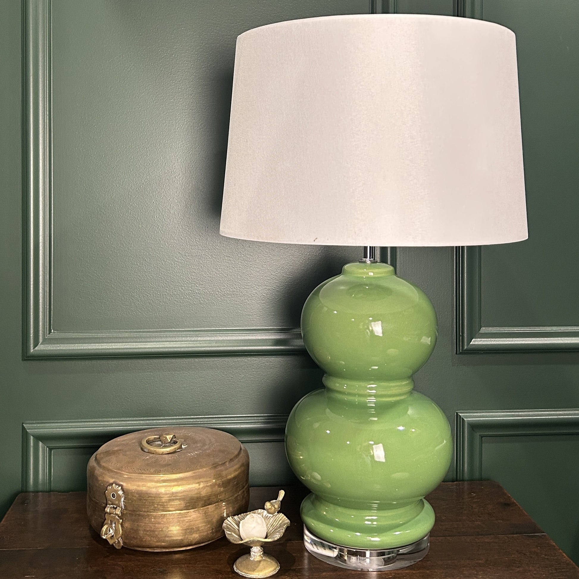 Green lamp with a white shade on a wooden surface against a green wall