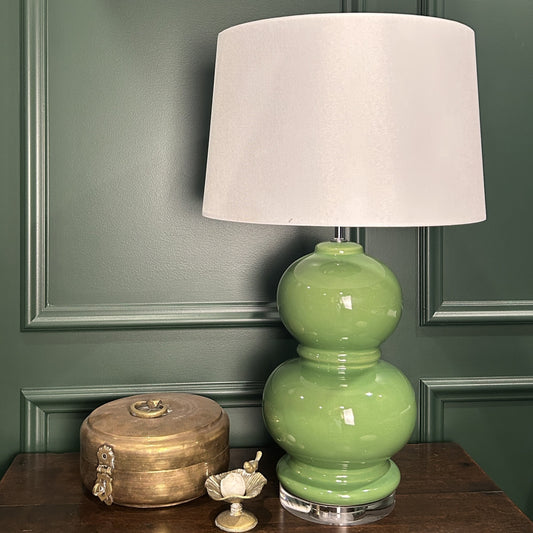 Green lamp with a white shade on a wooden surface against a green wall