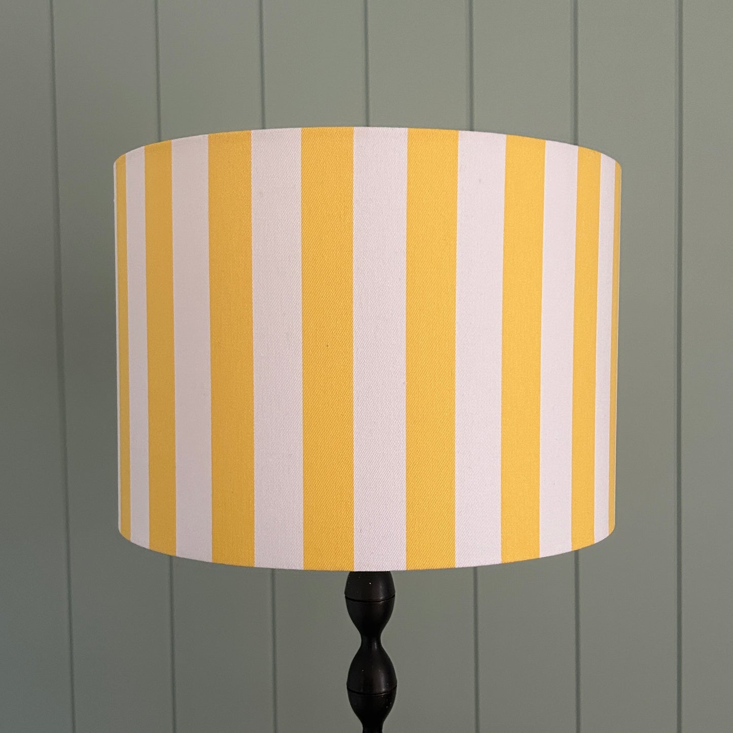 Striped lampshade with yellow and white stripes on a lamp stand against a panelled wall