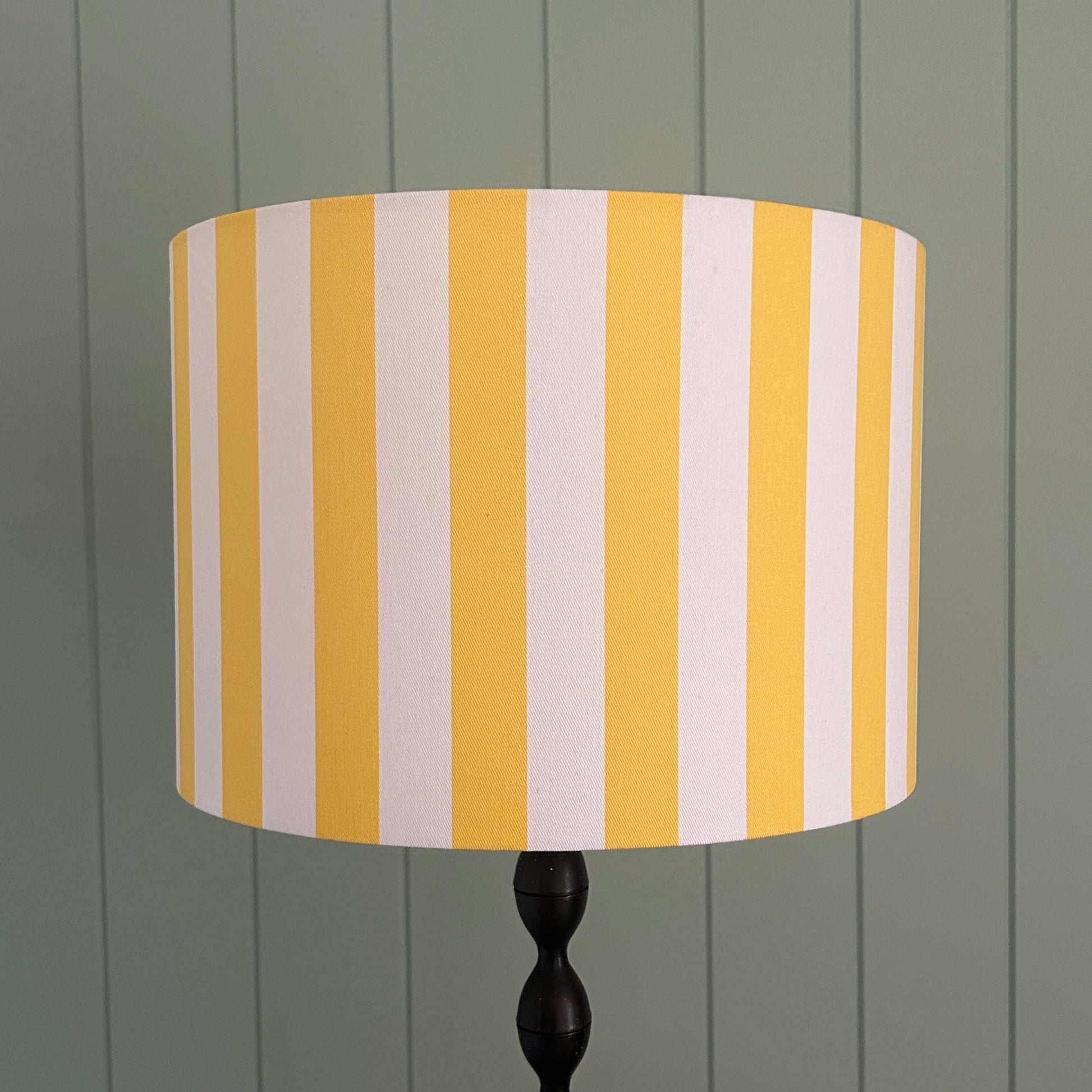 Striped lampshade with yellow and white stripes on a lamp stand against a panelled wall