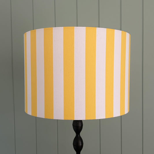 Striped lampshade with yellow and white stripes on a lamp stand against a panelled wall
