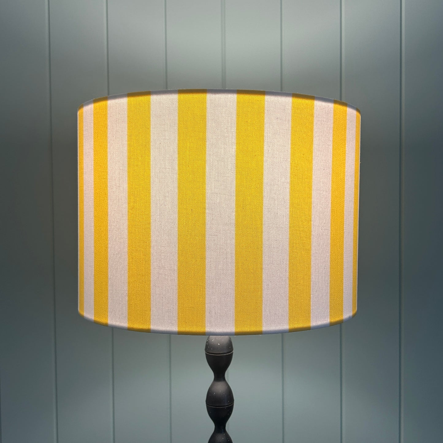 Striped yellow and white lampshade shown lit by light, on a lamp stand