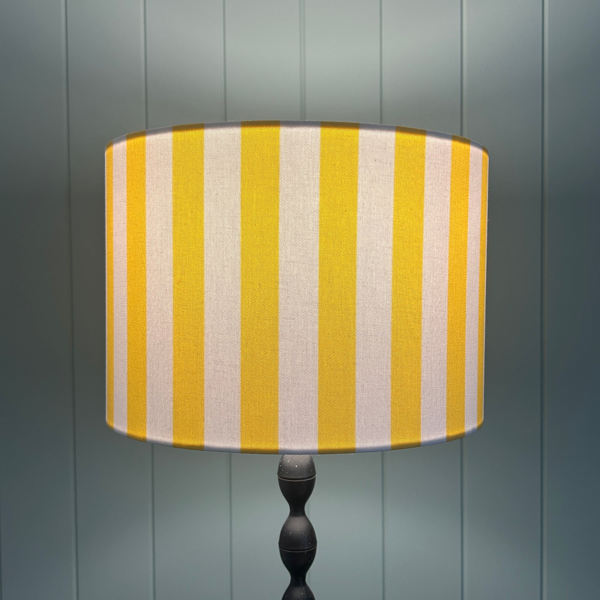 Striped yellow and white lampshade shown lit by light, on a lamp stand